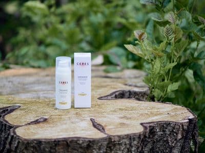 Eine Flasche und eine Verpackung des CERES Centaurium Naturkosmetikprodukts stehen auf einem Baumstumpf im Freien, umgeben von grünen Pflanzen.