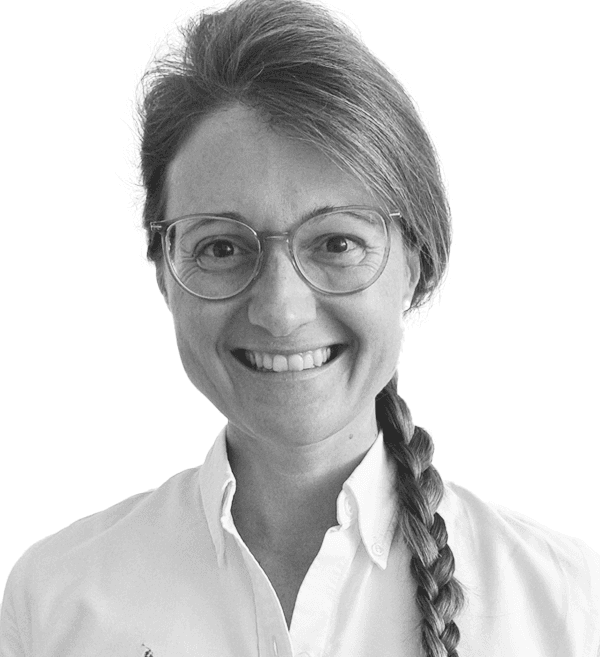 Fröhliche Frau mit geflochtenem Haar und Brille, die in weißer Kleidung lächelt vor weißem Hintergrund.